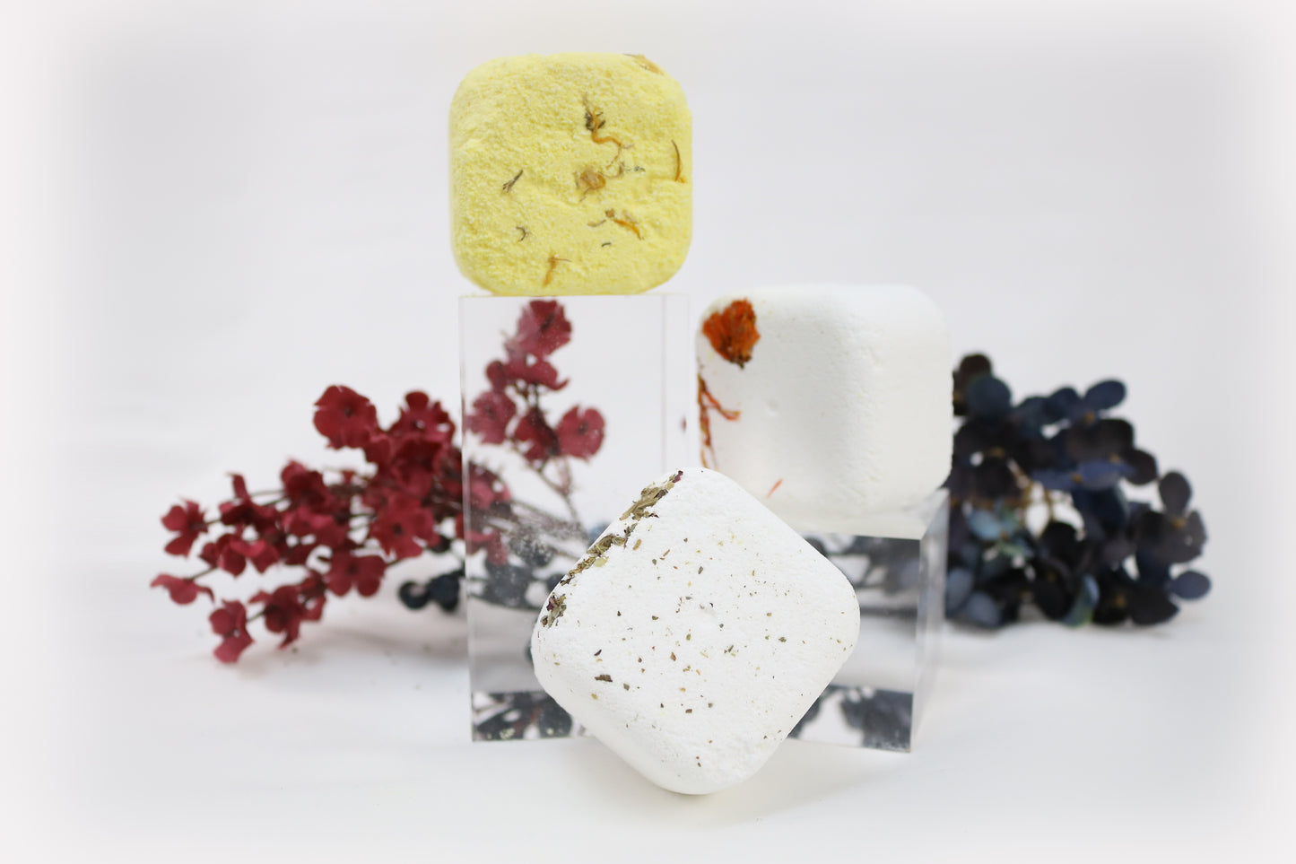 Stacked solid shower steamers in yellow and white, photographed with dried floral accents on a clean white background.