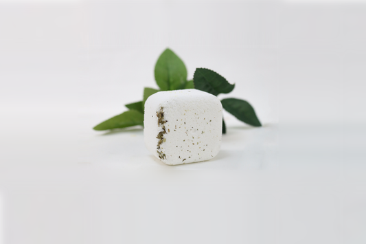 A white shower steamer with speckles, placed on a white surface with a green leaf partially visible to the side.