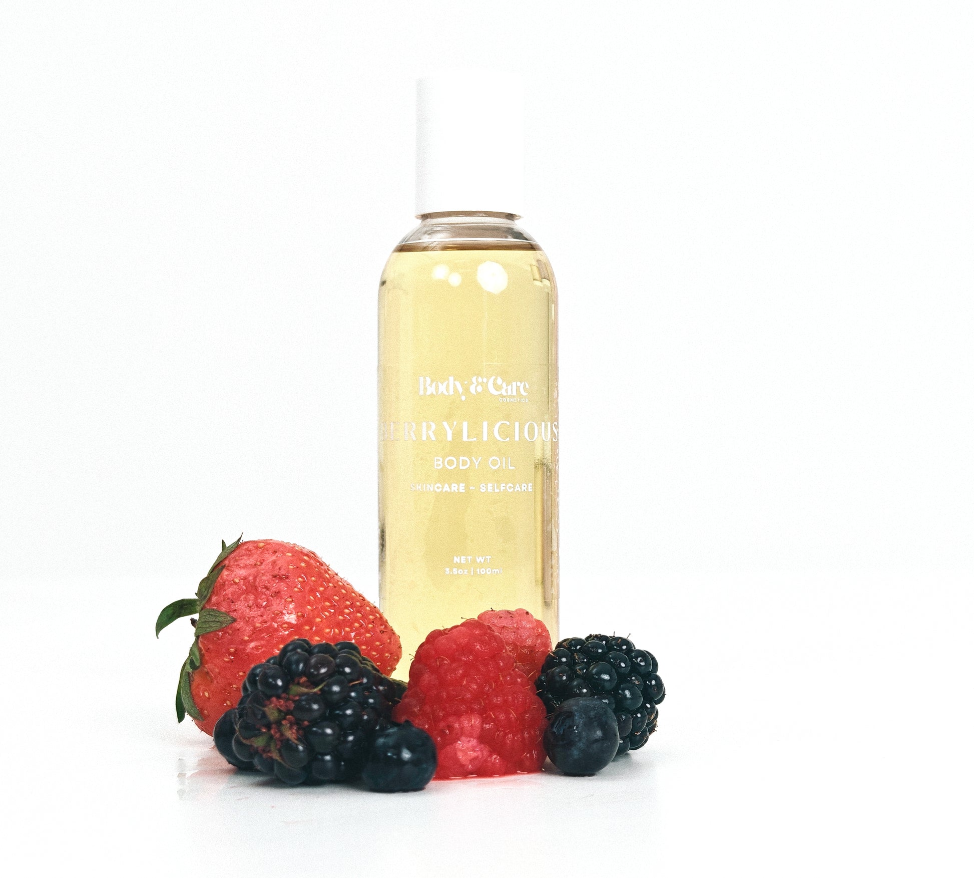 Body & Care Berrylicious Body Oil in a clear bottle with white cap, styled with mixed berries on a white background.