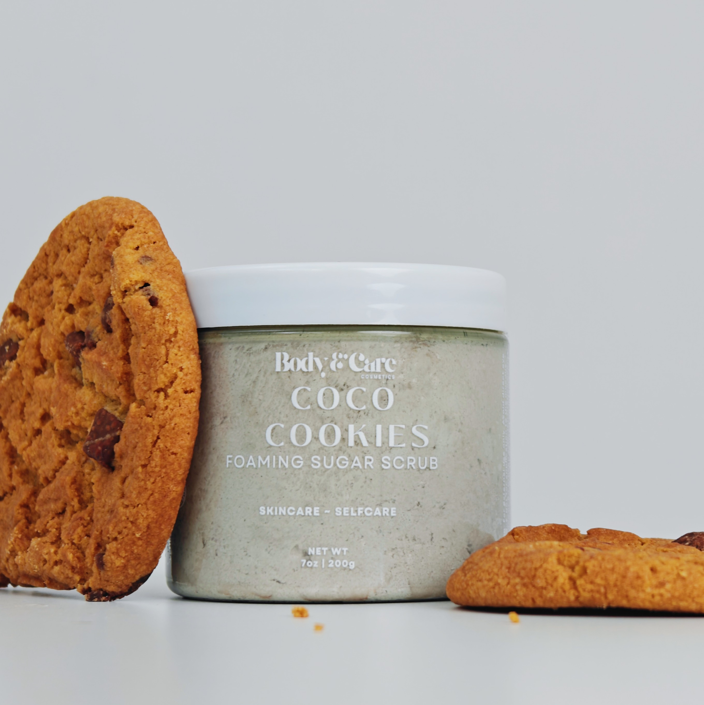 Body & Care Coco Cookies Foaming Sugar Scrub styled with chocolate chip cookies on a light background.