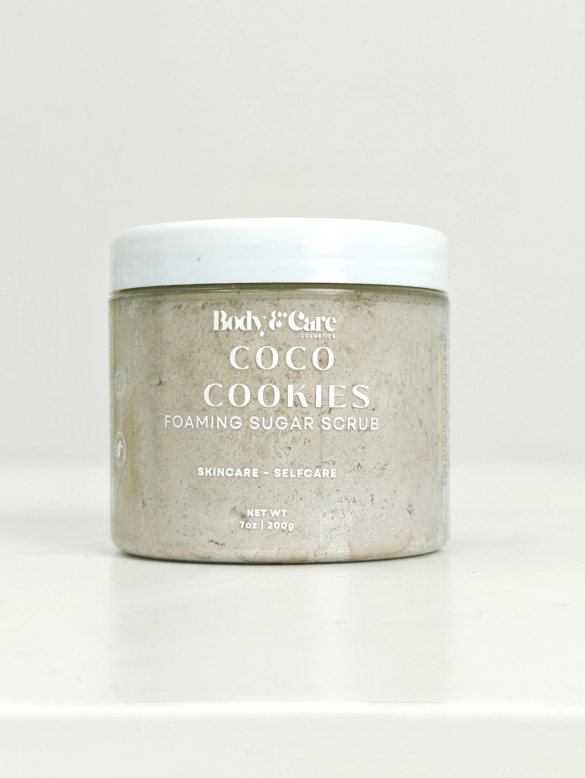 Body & Care Coco Cookies Foaming Sugar Scrub in a clear jar with white lid on a white background.