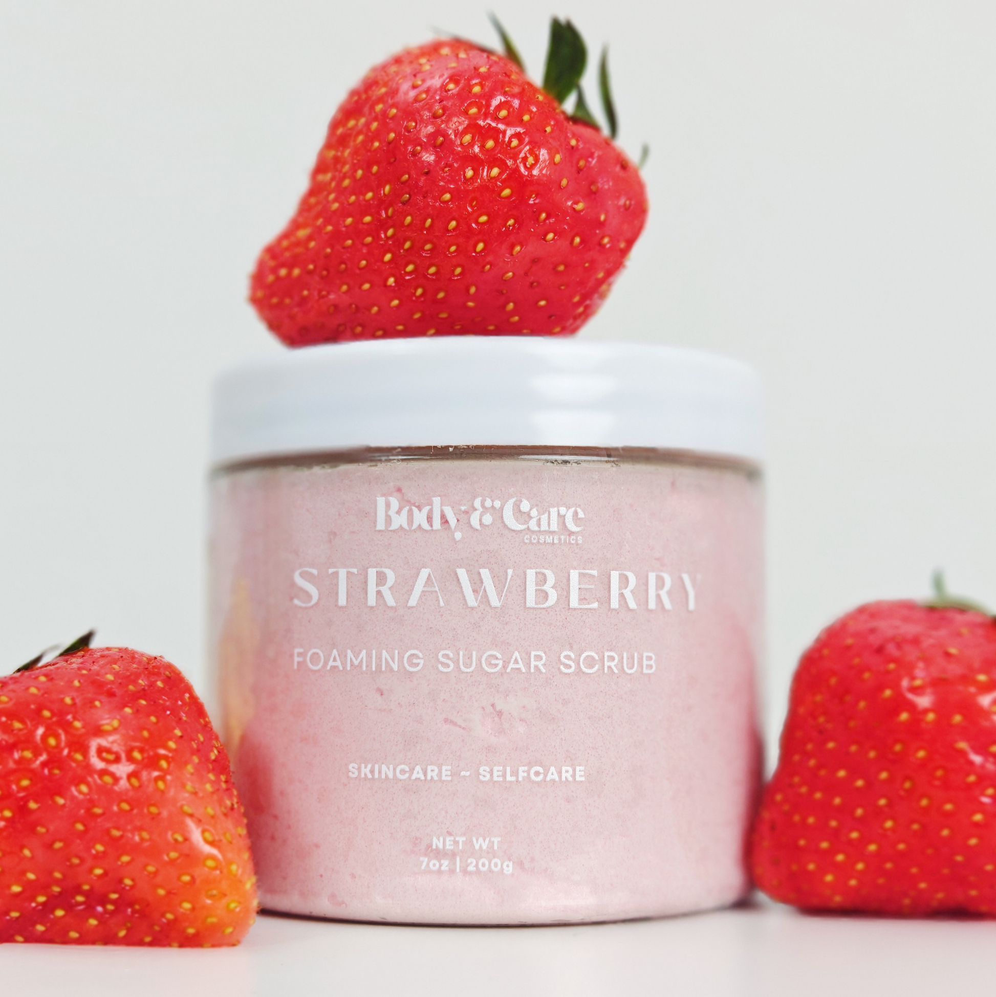 Body & Care Strawberry Foaming Sugar Scrub styled with fresh strawberries on a light background.