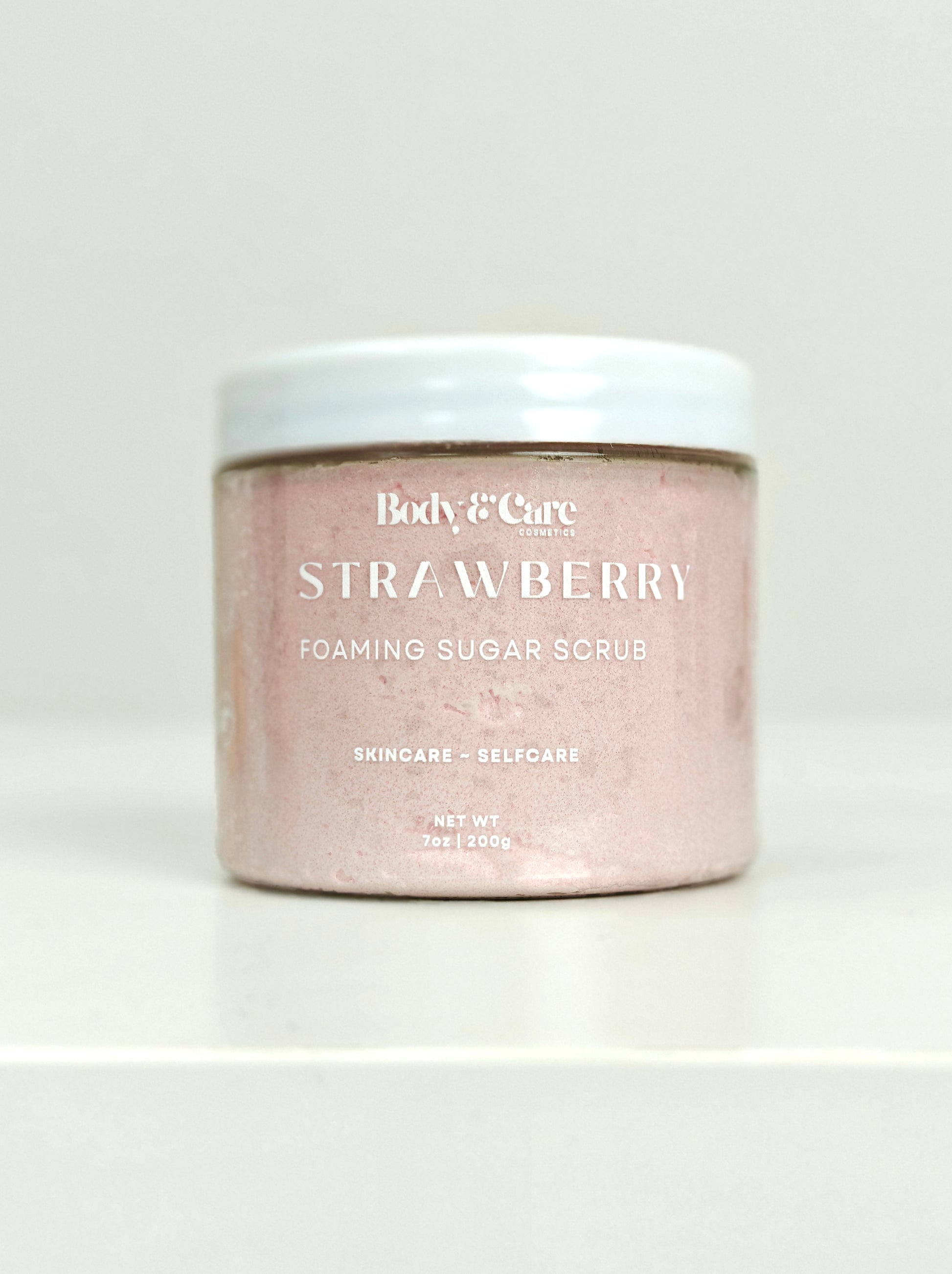 Body & Care Strawberry Foaming Sugar Scrub in a clear jar with white lid on a white background.