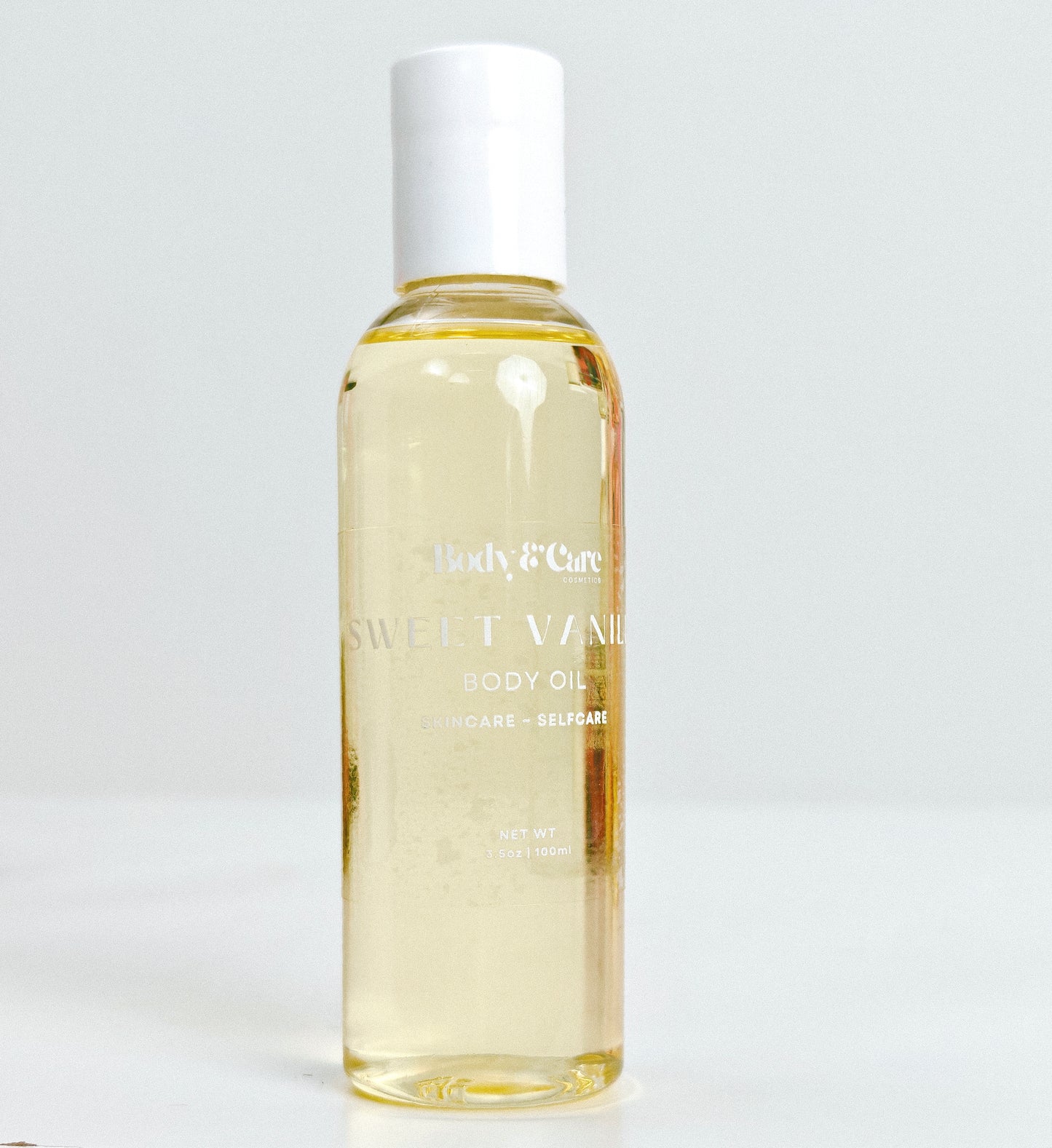 Body & Care Sweet Vanilla Body Oil in a clear bottle with white cap on a light background.